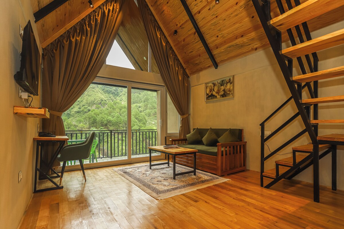 A spacious loft-style room with a wooden ceiling, a green sofa, a wooden table, and a staircase.