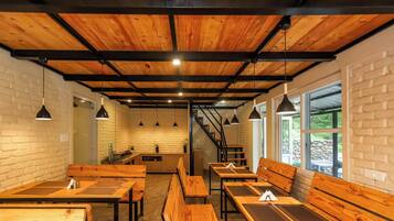 A restaurant interior with wooden tables and benches, brick walls, and a staircase leading to a kitchen area.