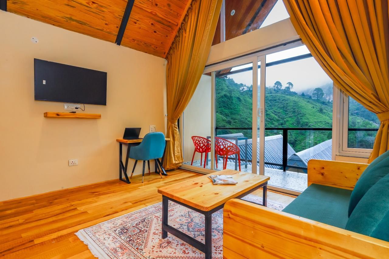 A room with a wooden ceiling, a flat-screen TV mounted on the wall, a table with a cushion, and a sofa.