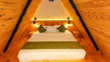 Une pièce triangulaire en bois, comprenant un lit, deux tables de chevet et des lampes fixées au mur.