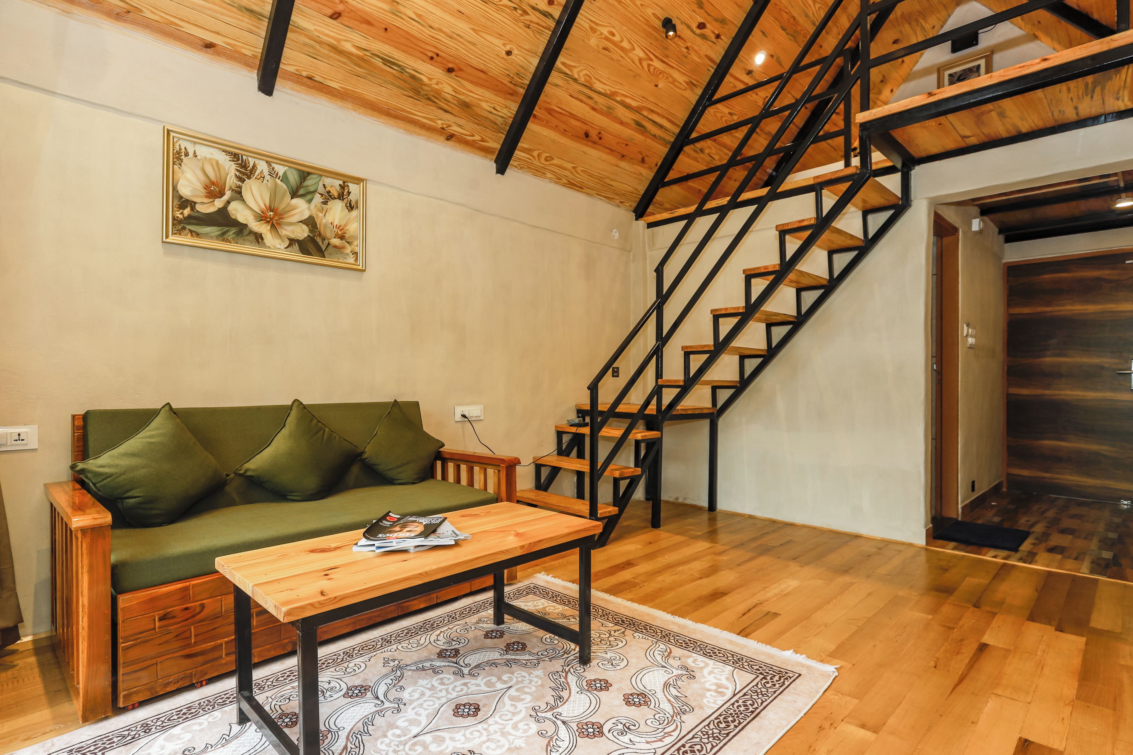 Uma sala de estar com escada de madeira, sofá verde, mesa de centro de madeira e tapete estampado.