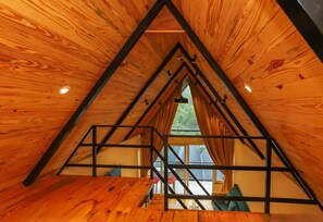 Un dormitorio abuhardillado triangular con paredes de madera y una escalera de metal.