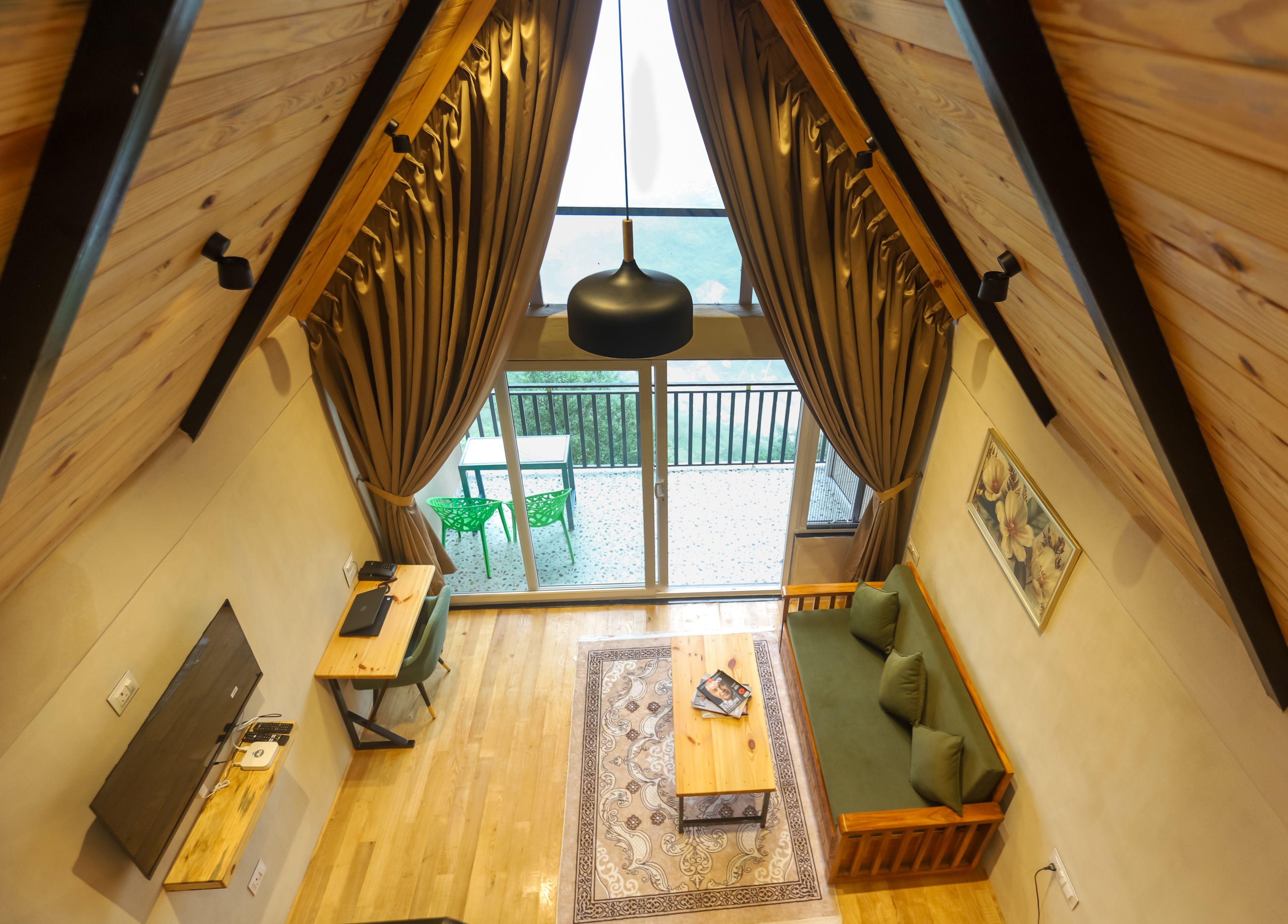 A room with a wooden ceiling, a sliding glass door leading to an outdoor balcony, a green sofa, a wooden table, and a small rug.