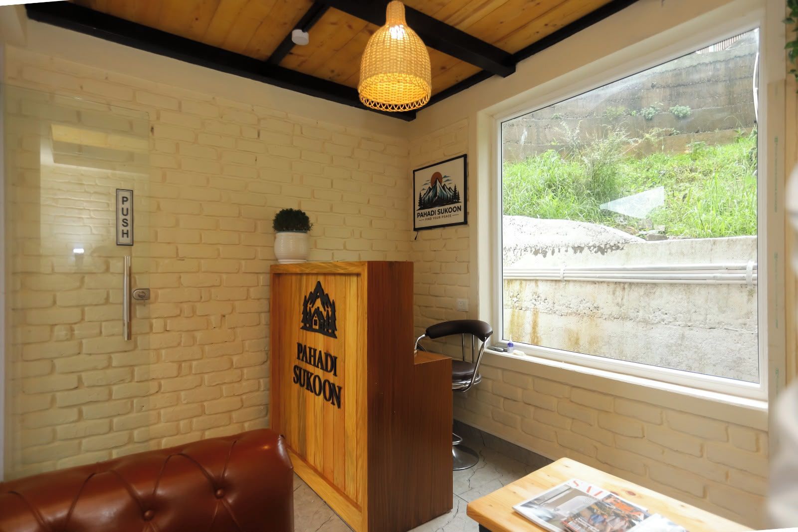 A room with a wooden cabinet labeled 'PAHADI SUKOON,' a bench, a chair, a table with a magazine, a window with a view of greenery, and a 'PUSH' sign on the wall.