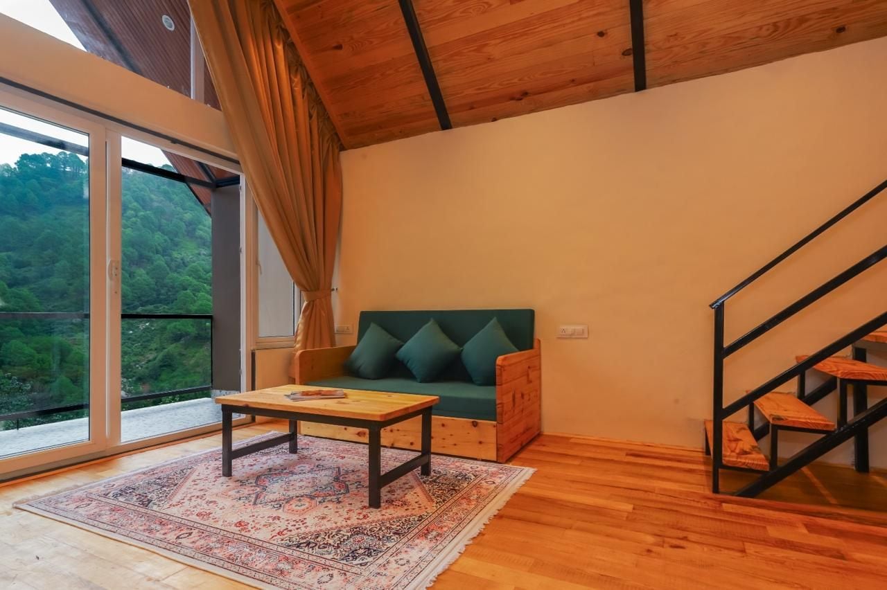 A room with a wooden floor, a green sofa with cushions, a small table, and a staircase.