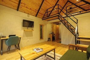 A room with a wooden floor, a desk with a chair, a television mounted on the wall, and a staircase with a metal railing.