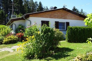 Ein eingeschossiges Haus mit Ziegelaußenwand, einem kleinen Vorgarten mit verschiedenen Pflanzen und Blumen sowie einem klaren Himmel.