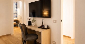 A modern room with a flat-screen TV mounted on the wall, a wooden desk, a grey chair, and a small plant on the desk.