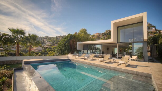 Una casa moderna con piscina, sillones de descanso y vistas del paisaje circundante.