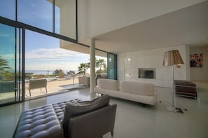 A modern living room with a large window, a sofa, a leather ottoman, and a flat-screen TV. - Other (Vallauris)