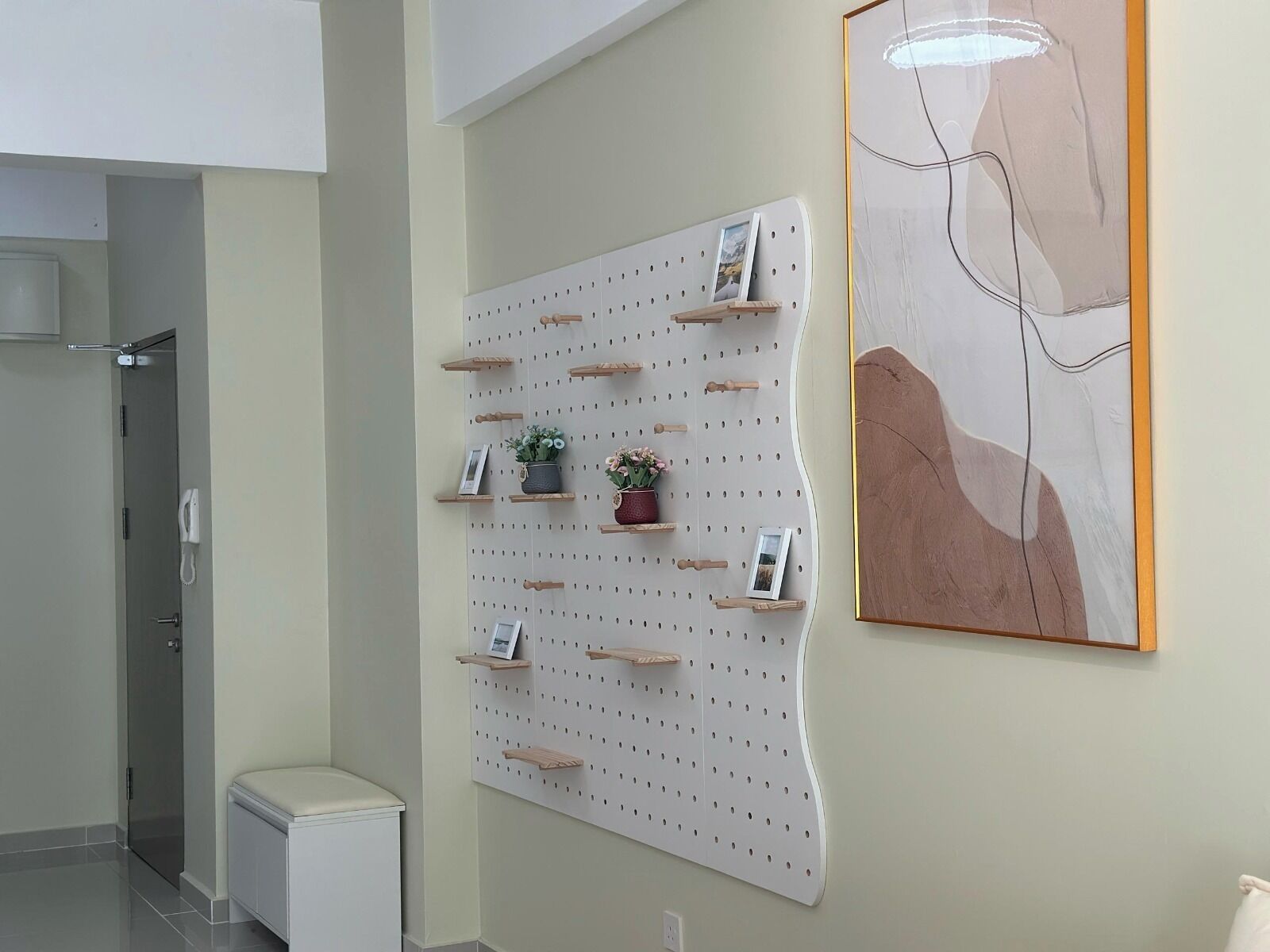 A wall-mounted pegboard with hooks and shelves, a framed abstract painting, and a small white cabinet.