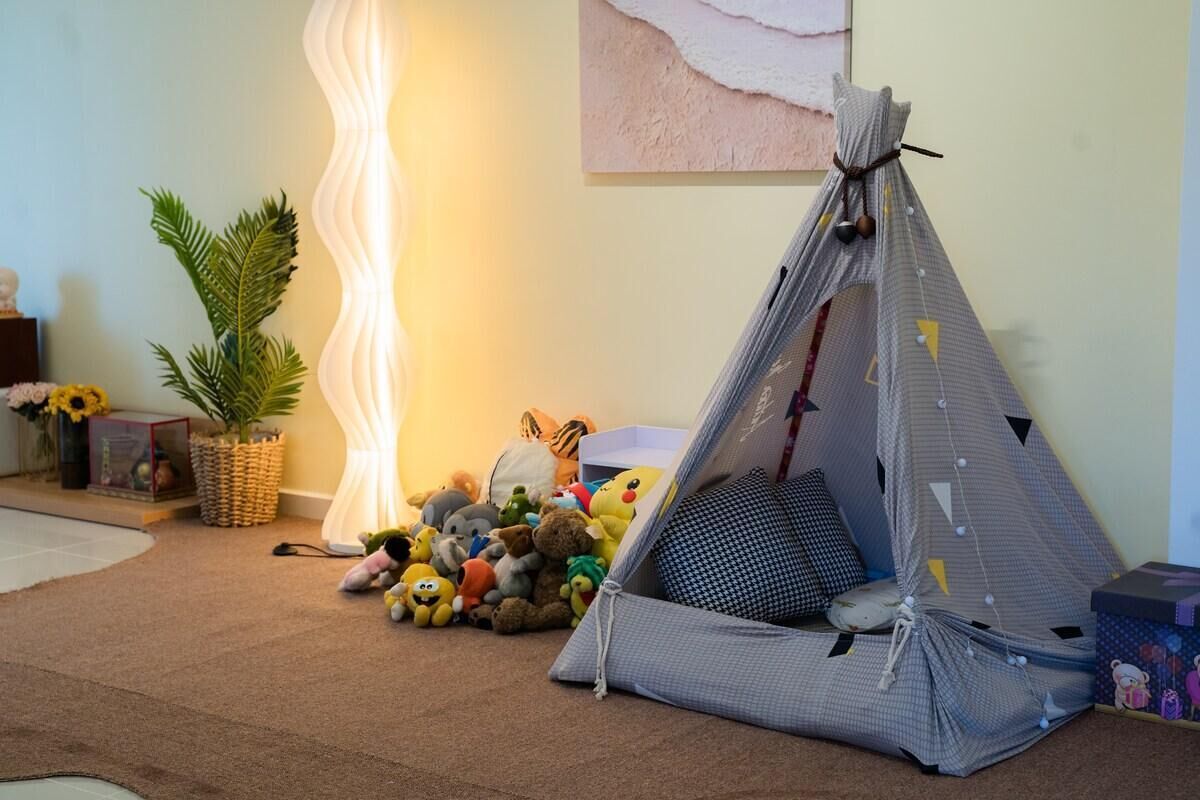 A cozy room with a sleeping area featuring a tent-like structure, a lamp, plush toys, and a potted plant.