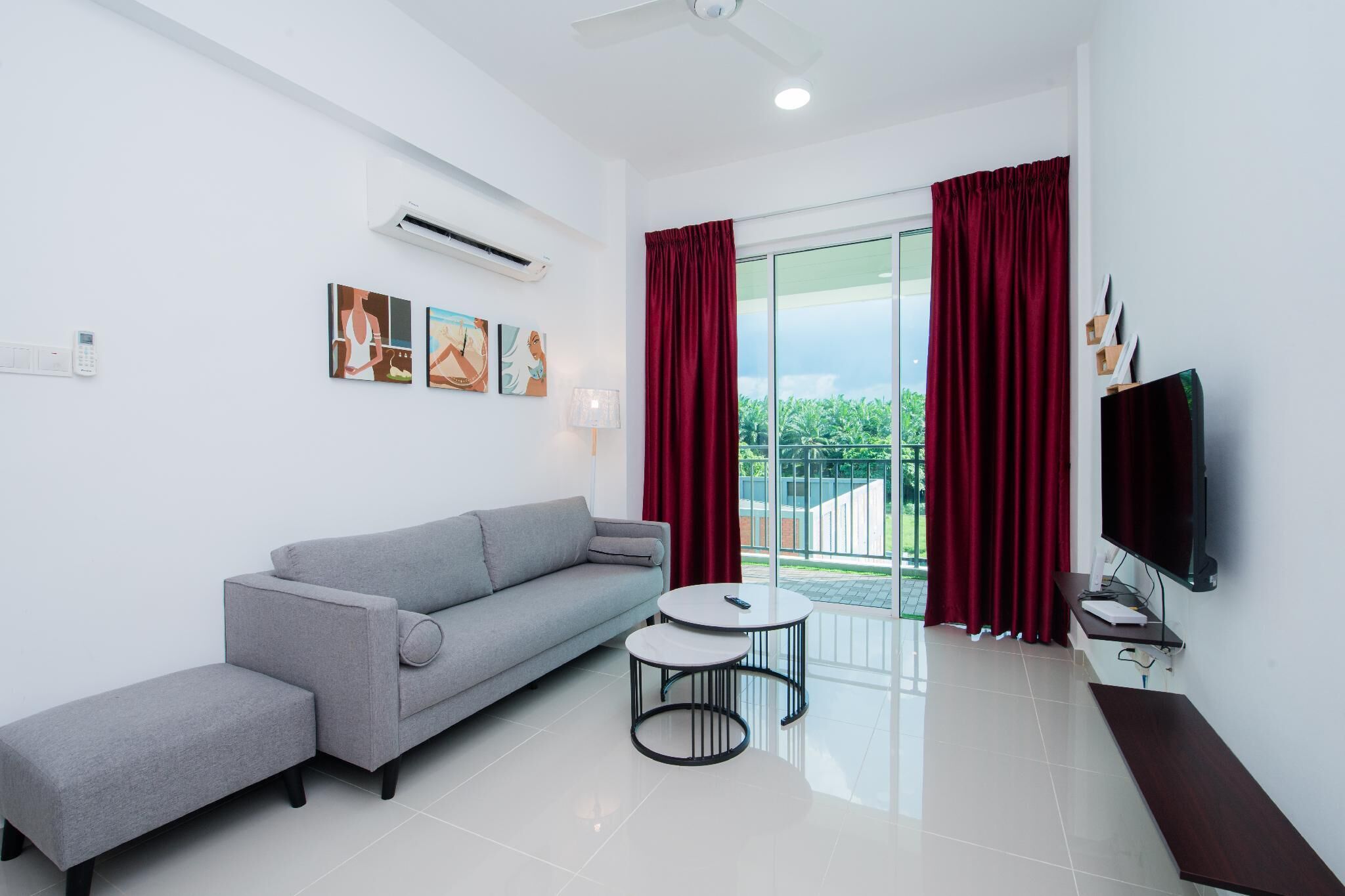 A modern living room with a grey sofa, a small round table, a TV, and a balcony with red curtains.