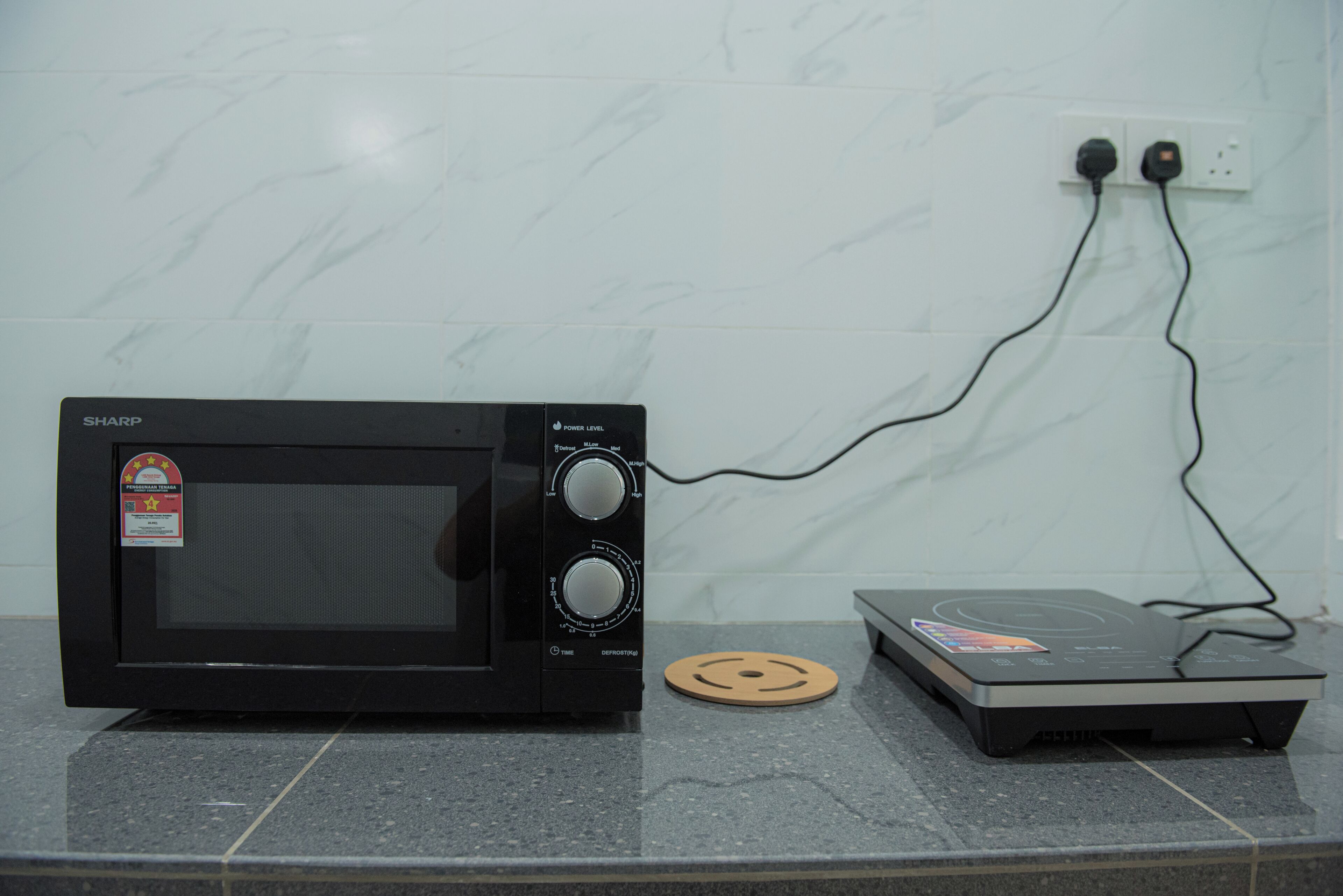 Un horno microondas conectado a una regleta eléctrica sobre una encimera de baldosas.