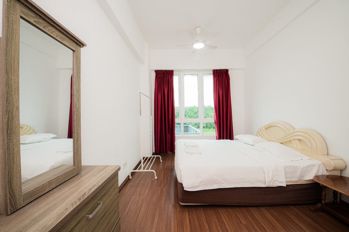 A bedroom with a bed, a large mirror, a ceiling fan, and a window with curtains.