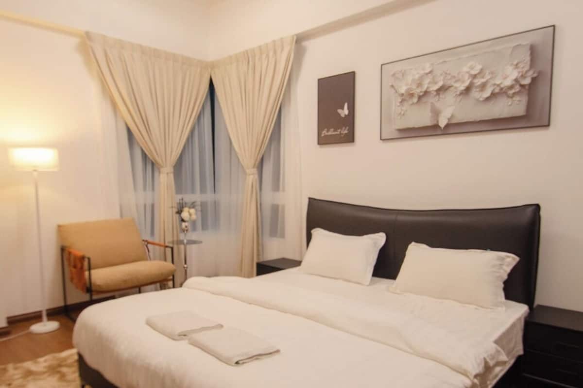 A hotel room with a large bed, a chair, a desk, a lamp, and artwork on the walls.