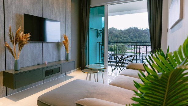 Una sala de estar moderna con una televisión de pantalla plana, un sofá, una mesita y un balcón con vistas a una zona boscosa.