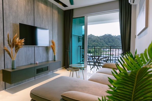 Una sala de estar moderna con una televisión de pantalla plana, un sofá, una mesita y un balcón con vistas a una zona boscosa.