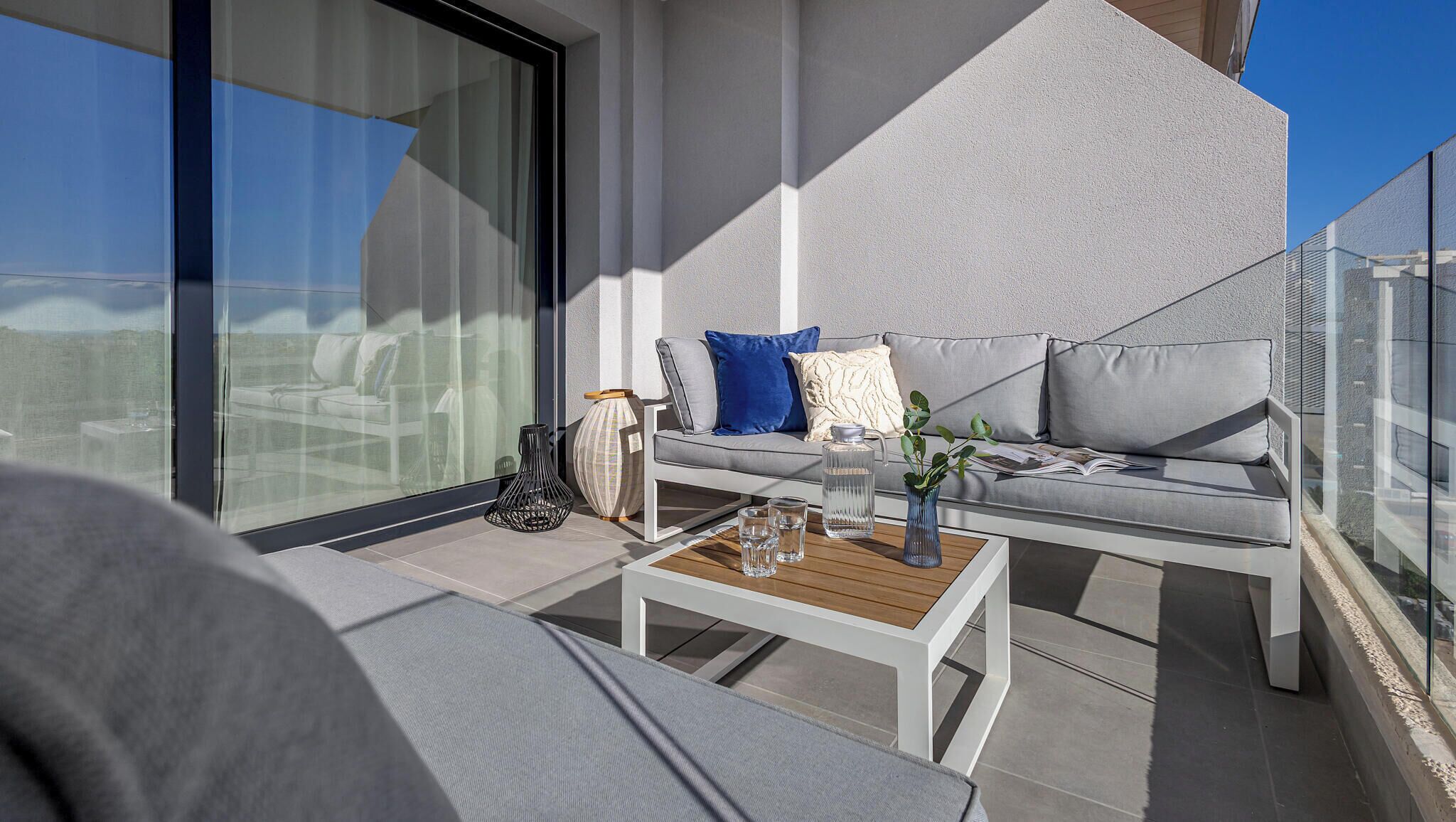 Un balcon moderne avec un canapé, une table basse et une rambarde en verre.