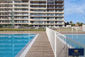 Um hotel moderno com uma piscina grande, várias varandas e uma área externa bem cuidada.