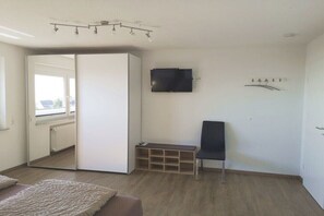 Ein Zimmer mit einer Schiebetür, einem an der Wand befestigten Fernseher, einer Bank und einem Sessel.