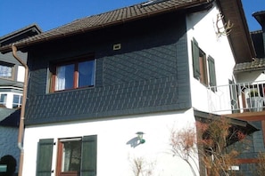 Ein zweistöckiges Gebäude mit dunklen Schindeldächern, einem Balkon mit Geländer und einem kleinen Fenster mit Fensterläden.
