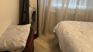 Ein Schlafzimmer mit einem Bett, einem Nachttisch, einem Spiegel und einem Fenster mit durchsichtigen Vorhängen.