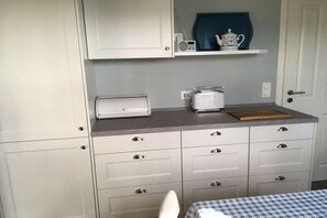 A kitchen with white cabinets, a microwave, a toaster, and a blue and white checkered tablecloth. - "House at Brockeswald" (Cuxhaven)