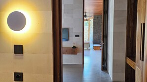 A modern interior with a hallway leading to a room, a circular light fixture on the wall, and a wooden ceiling.
