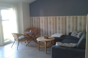 Ein Wohnzimmer mit einer Couch, einem kleinen Tisch, einem Sessel und einer gestreiften Wand.
