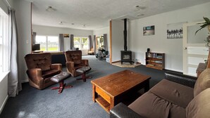 A spacious living room with leather sofas, a wooden coffee table, a fireplace, and a bookshelf. - Cliff Top Homestead - great for couples, friends, families and large groups (Ōhingaiti)