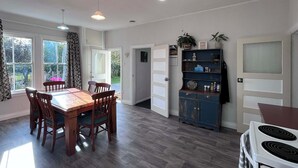 A dining area with a wooden table and chairs, a built-in cabinet, and a view of the garden through large windows. - Cliff Top Homestead - great for couples, friends, families and large groups (Ōhingaiti)