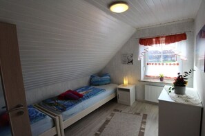 Ein kleines, einzelnes Zimmer mit einem Etagenbett, einem Nachttisch mit Lampe, einem Fenster mit Vorhängen und einer Heizung.