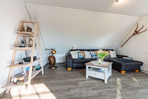 Ein Loft-Wohnraum mit Holzleiter, einer schwarzen Couch mit gemusterten Kissen, einem weißen Couchtisch und einer dekorativen Lampe.