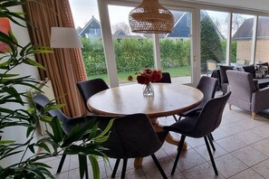 A dining area with a round table, chairs, a vase with flowers, a lamp, and a view of the garden through large windows. - Holiday home with 2 bedrooms (Sint Maarten)