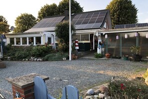 Ein Haus mit Solaranlage, einem Backsteinkamin und einem Garten mit Topfpflanzen.