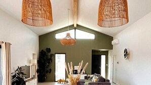 Ein Essbereich mit Holztisch und Stühlen, zwei hängenden Korbstühlen und Blick in ein Wohnzimmer mit Sofa und Pflanze.