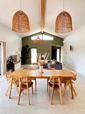 A dining area with a wooden table and chairs, two hanging wicker lamps, and a view into a living room with a sofa and a plant. - Villa between the Landes forests and ocean (Seignosse)
