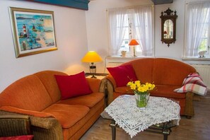 Ein Wohnzimmer mit zwei orangenen Sofas, einem Tisch mit wei ßer Spitzenleinentischdecke und einem Bild an der Wand.