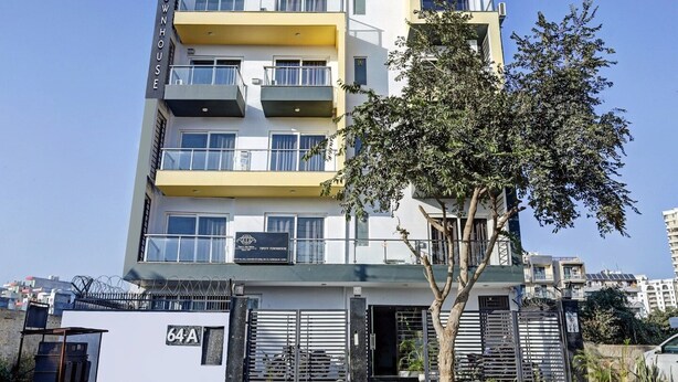Um edifício residencial com vários andares, varandas, portão fechado e uma árvore em primeiro plano.