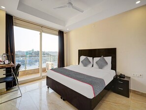 A hotel room with a bed, a desk, a chair, a nightstand, and a view of the city. - Townhouse Tipsyy Near Bestech Central (Gurugram)