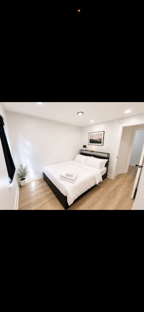 Ein modernes Schlafzimmer mit einem Bett, einer Zimmerpflanze und einem gerahmten Bild an der Wand.