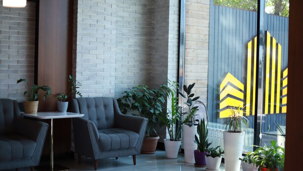 Un intérieur moderne avec un mur en briques, des canapés gris, une petite table et diverses plantes en pot.