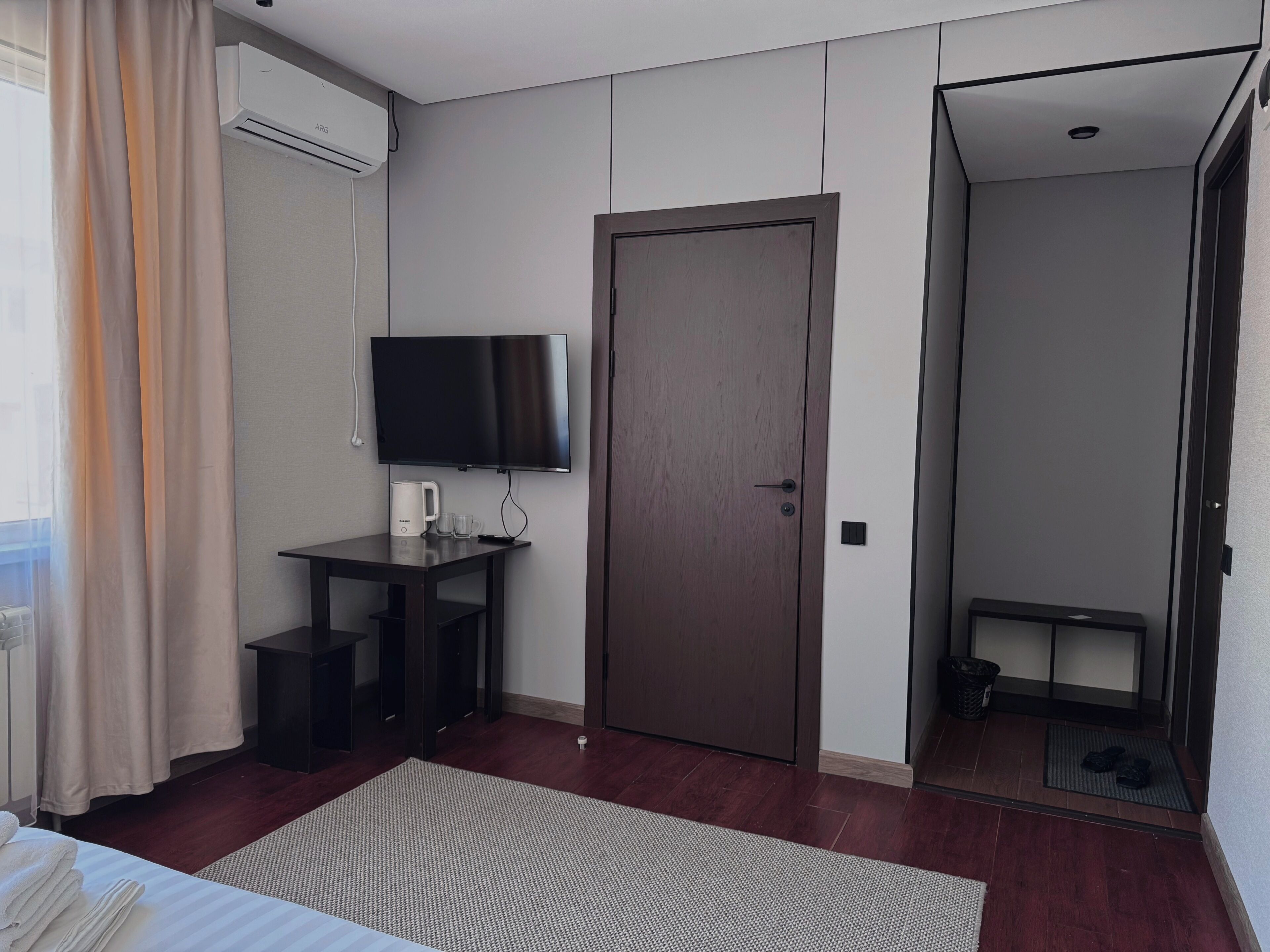 Habitación de hotel con cama, escritorio con televisor, puerta y vista al exterior.