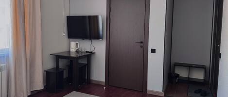 Habitación de hotel con cama, escritorio con televisor, puerta y vista al exterior.