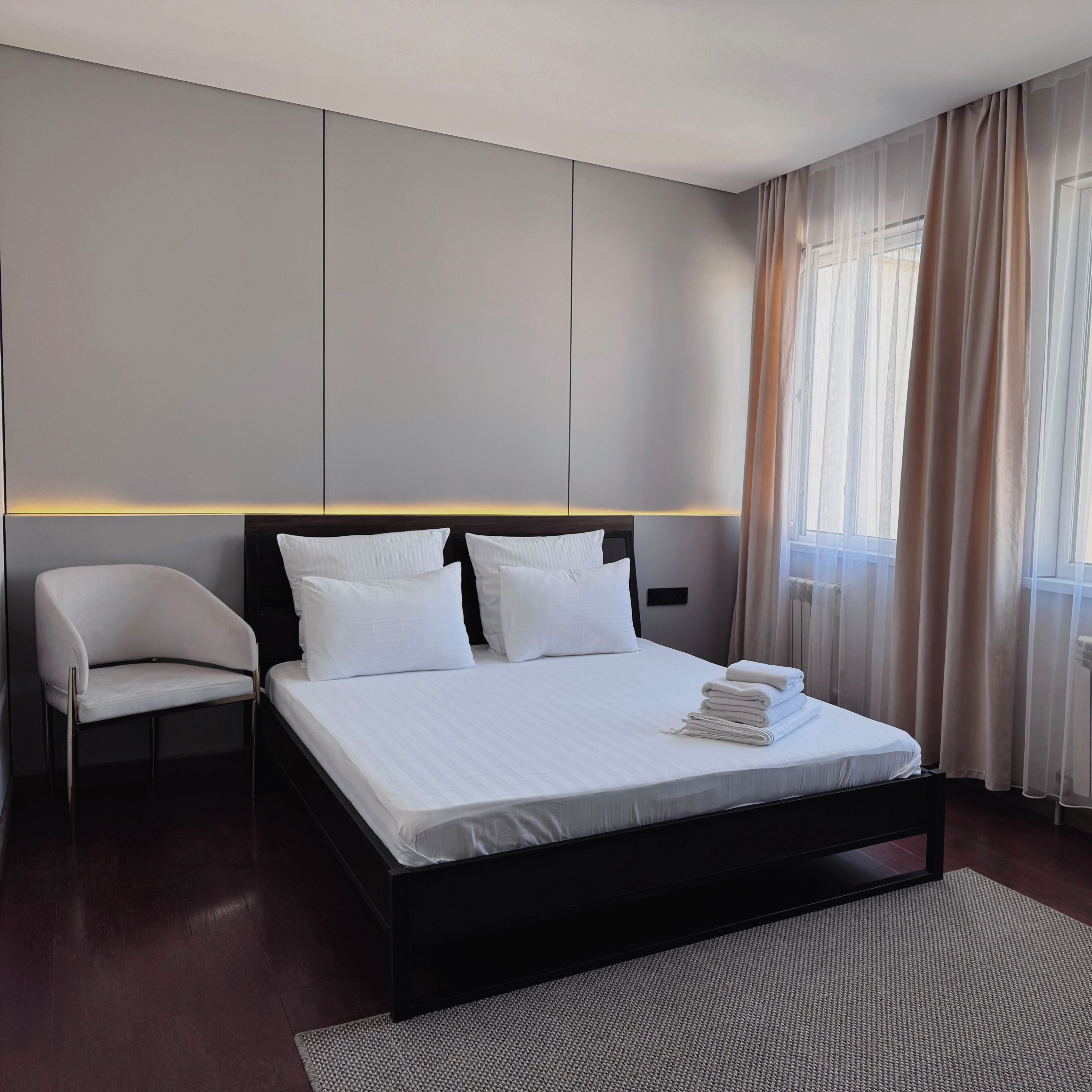 A modern hotel room with a large bed, a chair, and a view of the outdoors.