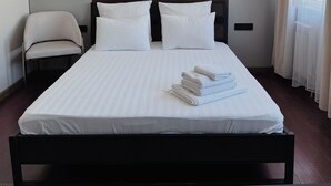 Un lit bien fait, avec du linge de lit blanc, une chaise et une table de chevet, dans une chambre d’hôtel moderne.
