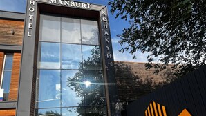 Une entrée d’hôtel moderne avec une grande façade en verre, une façade en bois d’un côté et un logo sur la droite.