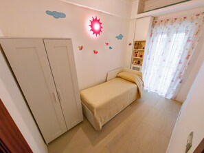 Ein kleines, aufgeräumtes Schlafzimmer mit einem Einzelbett, einem Kleiderschrank und einem Regal mit Dekoration.