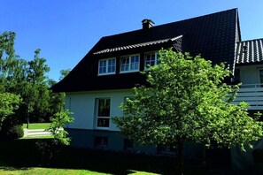 A two-story house with a dark roof, white walls, and a large tree in front. - Holiday apartment with 1 bedroom (Detmold)
